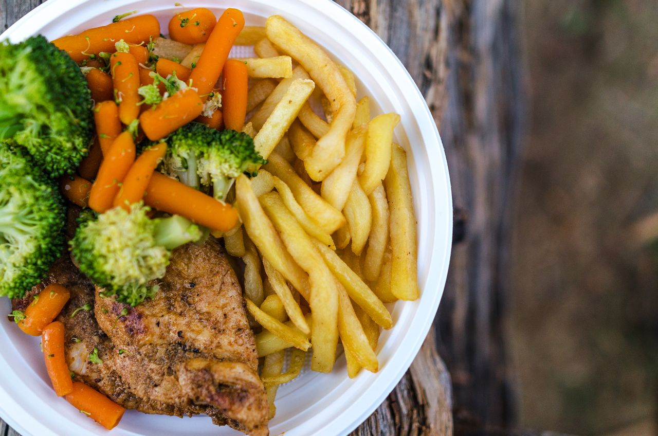 Services Delicious chicken dinner with broccoli, carrots, and fries on a plate.