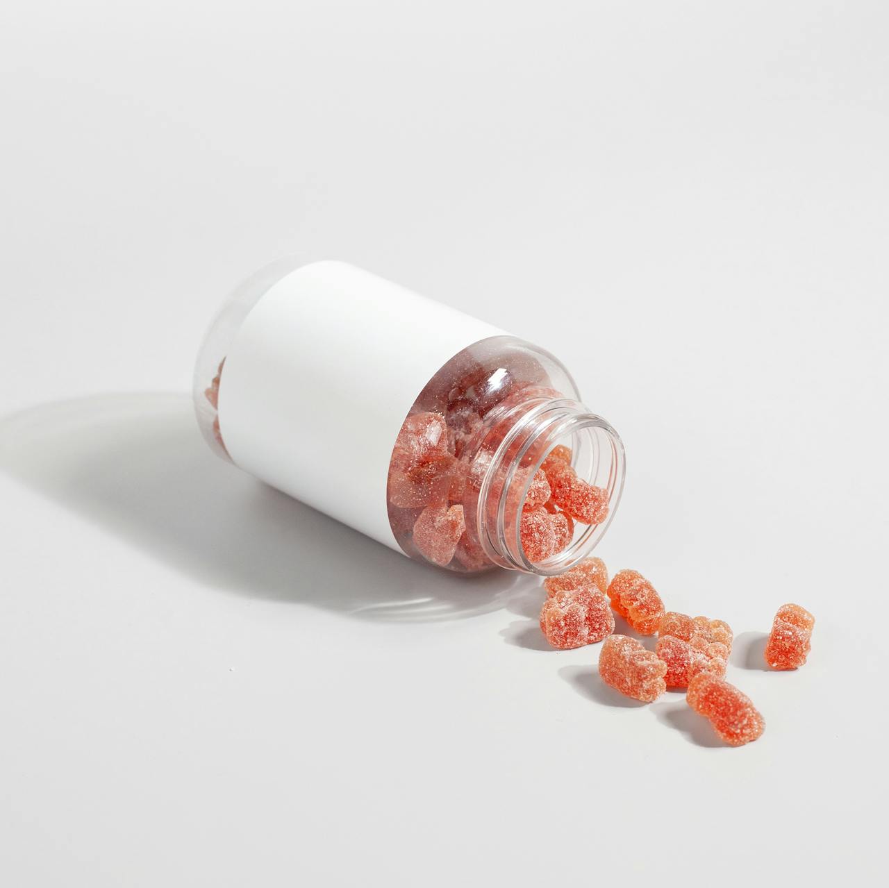 Services Close-up of gummy vitamins spilled from a clear bottle on a white surface